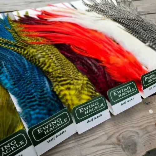 Colorful fishing fly hatches with Ewing Hackle labels on a wooden surface